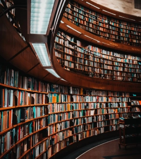 An elegant, curved library with floor-to-ceiling bookshelves filled with books. The warm lighting and wooden accents offer a cozy reading environment in the Dosti West County, Thane Balkum.